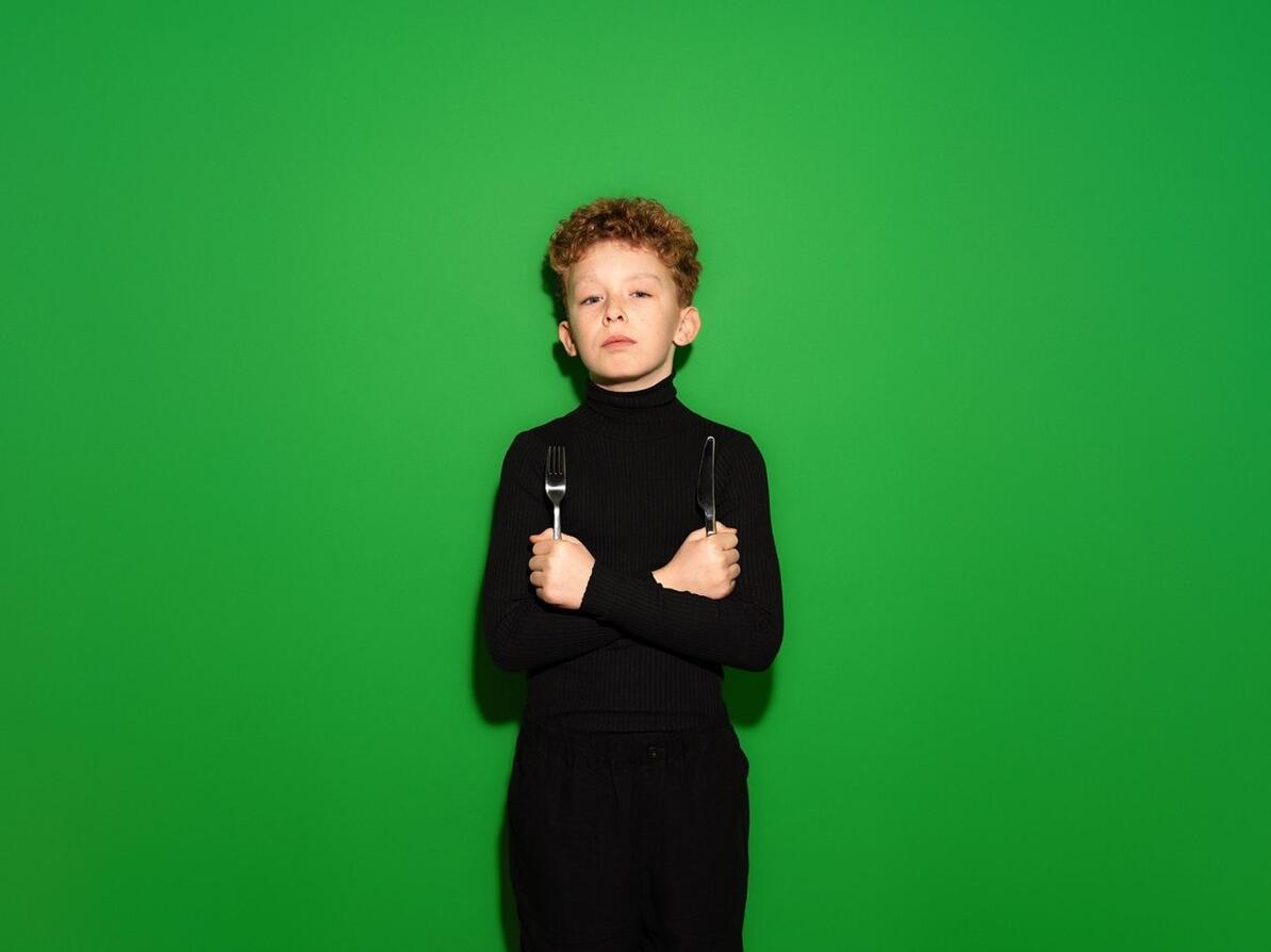 Dreng på grøn baggrund med kniv og gaffel i hånden